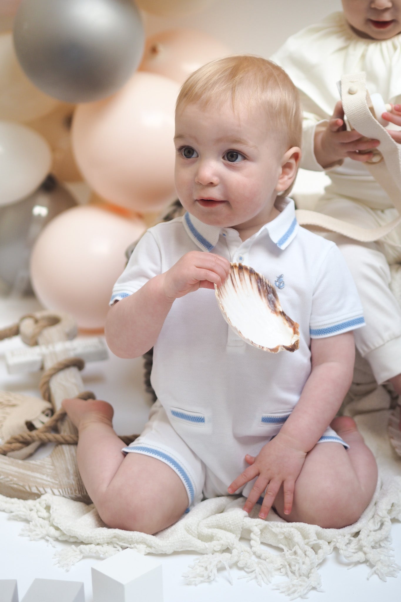 baby boy in romper holding shell